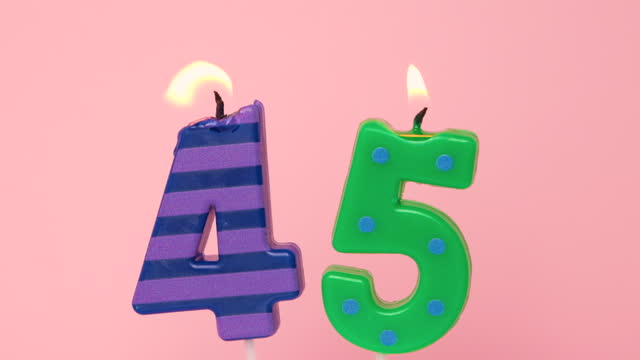 Forty five years Anniversary video banner with Burning spotted green and striped purple candles. Number forty five candle on light pink background. 4K resolution happy birthday banner.