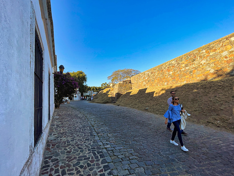 colonia del sacramento, uruguay - november 2 2022: tourists walking on cobble stone unesco world heritage site colonial street
