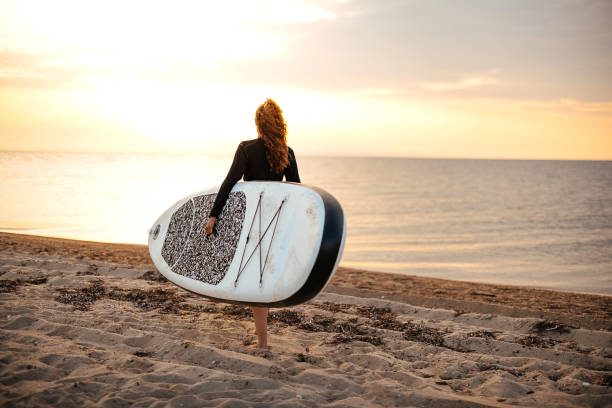 istock Woman standing on a beach ready to go paddle boarding 1905767547