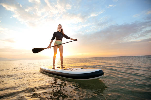 istock Young woman swimming on sup boards alone at sunset 1905768768