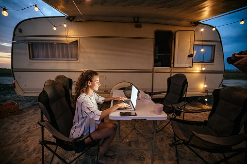 Woman working from a remote location while sitting next to the camper van