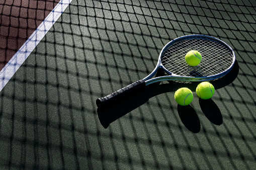 Tennis racket and three balls on an outdoor tennis court