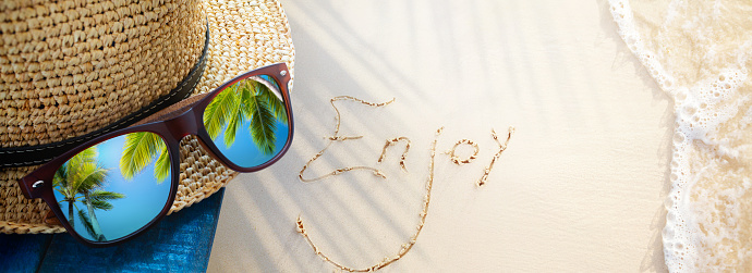 enjoy tropical holiday, tropic holidays banner. sand beach from above with straw bucket hat and sunglasses, palm trees reflection, summer vacation concept banner with copy space