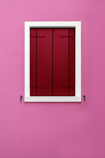 Decorated red smooth closed wooden window shutter with white frame on colorful pink wall background