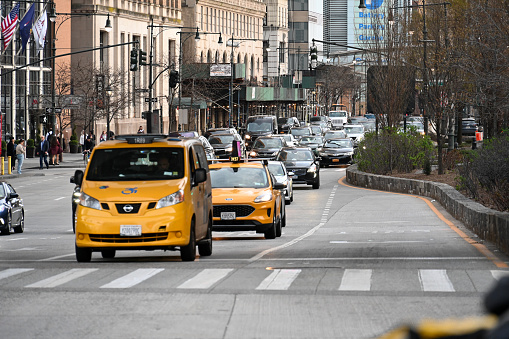 Woman hailing a yellow taxi on a busy street by Grand Central Terminal with American flags in the background