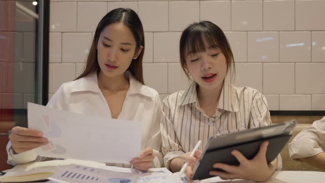 Young businesswomen discuss marketing plans inside a fast food restaurant.