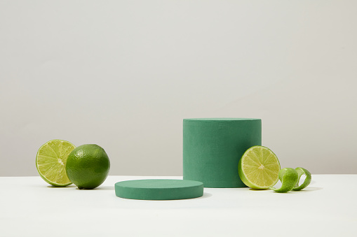 Two green display platforms and limes stand out against the white background. Product advertising concept with lemon extract as the main ingredient. Front view. Copy space.