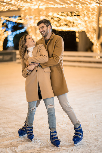 Close-up of young couple ice skating and embracing in skate ring while on a holiday.