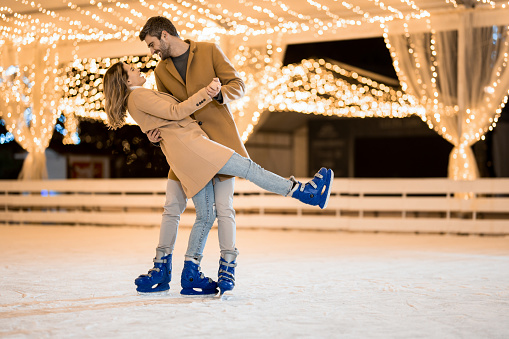 Joyful couple dancing on ice skates in the skating ring on a holiday.