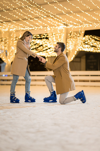 Happy young man proposing to his girlfriend while ice skating in the skate ring on a winter holiday.