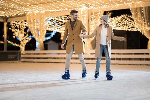 Joyful couple having a great time ice skating in the skate ring on a winter holiday.