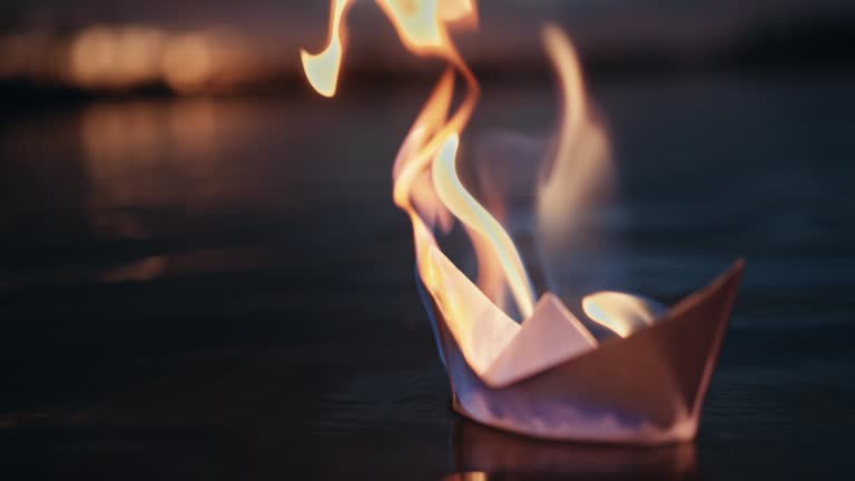 SLO MO Closeup of Burning Origami Paper Ship Floating on Lake with Ripples at Twilight