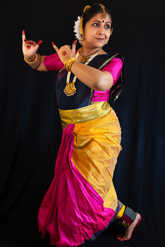 Indian female classical dancer in traditional costume performing Bharatanatyam dance on black background