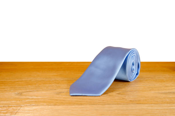 Plain fabric blue necktie rolled on wooden floor with white background close-up view single object concept copy space no people
