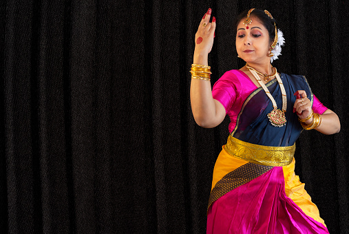 Indian classical dancer in traditional costume performing Bharatanatyam dance on black background