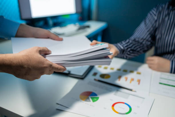 istock Hand a pile of important documents to a co-worker, Forward a summary of the previous month's meeting agenda to the department head, Big stack of documents 1906078009