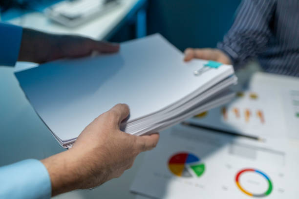istock Hand a pile of important documents to a co-worker, Forward a summary of the previous month's meeting agenda to the department head, Big stack of documents 1906079052