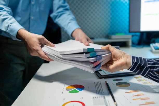 istock Hand a pile of important documents to a co-worker, Forward a summary of the previous month's meeting agenda to the department head, Big stack of documents 1906080580