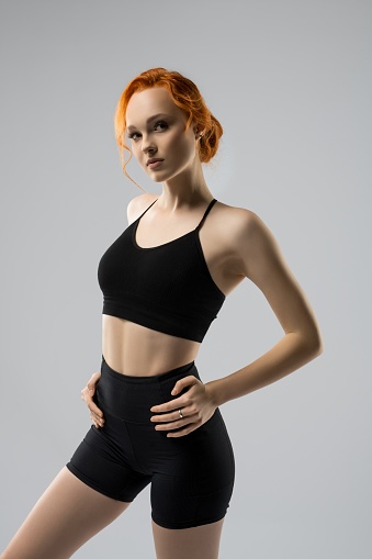 Self assured young fit female model with ginger hair in black sportswear serious look at camera