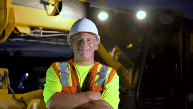 Construction worker standing by heavy machinery at night