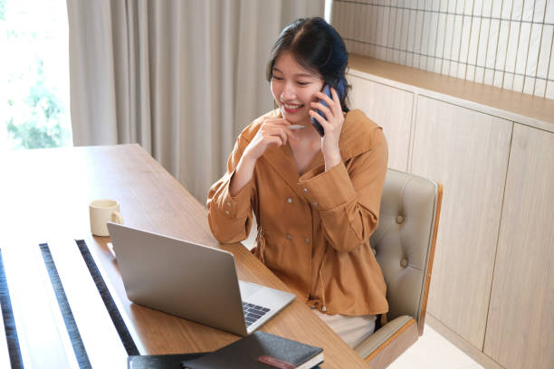 istock Beautiful businesswoman using a smartphone and working with a laptop while sitting at an office desk, working from home concept 1906130065
