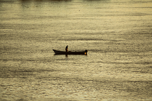 A fisherman, alone, on a small boat, at sunrise on the Parana river. On day May 5, 2023. In the Parana river, in front of the Rosario city, Santa Fe province, Argentina.