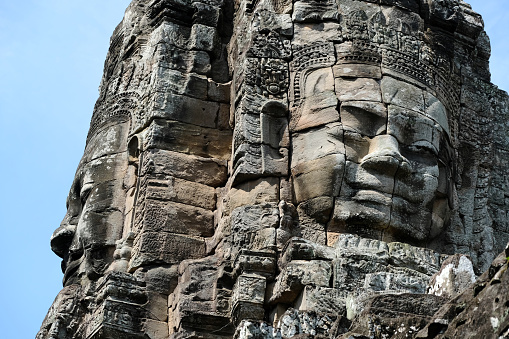 Stone faces at the Bayon, a richly decorated Khmer temple at Angkor in Cambodia. Built in the late 12th or early 13th century as the state temple of the King Jayavarman VII, the Bayon stands at the centre of Jayavarman's capital, Angkor Thom.\nThe Bayon's most distinctive feature is the multitude of serene and smiling stone faces of The Buddha.
