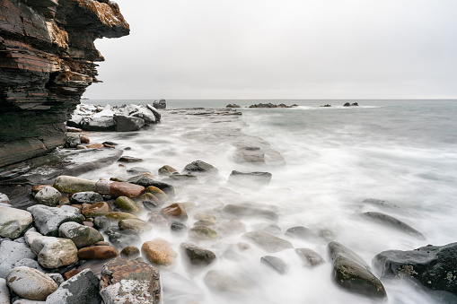 Rocky shores and waves of the Varangerfjord on a cloudy and gray day during the polar night, Ekkerøya, Northern Norway