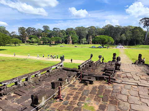 Group of tourists walking by the Terrace of the Elephants, part of the walled city of Angkor Thom, a majestic temple complex in Angkor, Cambodia. The terrace was used by Angkor's king Jayavarman VII as a platform from which to view his victorious returning army. The terrace is named for the carvings of elephants on its eastern face.