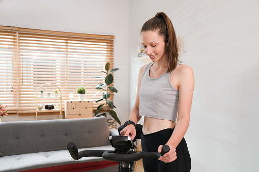 Beautiful sportswoman working out on on a smart exercise bike at home..