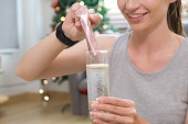 Young caucasian woman preparing healthy supplement after exercise dissolving collagen powder in glass of water.