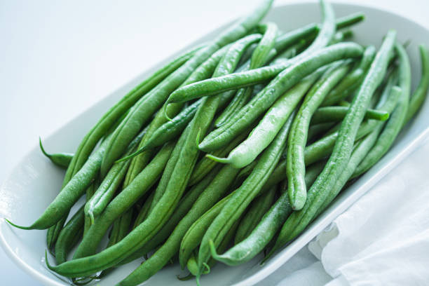 istock Raw fresh green beans on white plate, white background. 1906222012