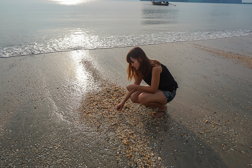 Woman collecting seashells on the beach. Woman picking up shells and holding them in hand on the beach.