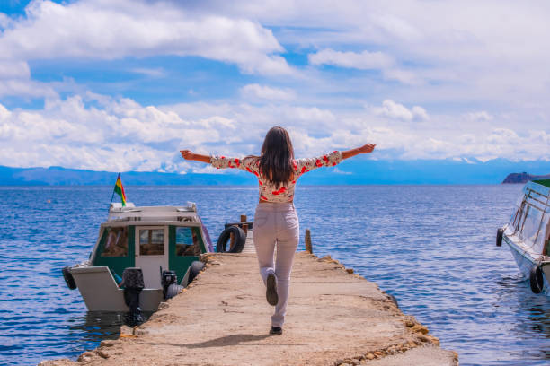 junge lateinamerikanische touristin mit erhobenen armen auf einem steg am ufer des titicacasees - bolivia copacabana bolivian ethnicity lake titicaca stock-fotos und bilder