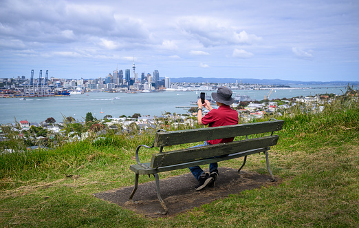 Tourist taking photos using smartphone of Auckland Sky Tower and skyline. Mt Victoria, Devonport. Auckland.