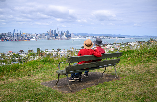 Couple sitting on the bench, enjoying the views of Auckland Sky Tower and skyline. Mt Victoria, Devonport. Auckland.