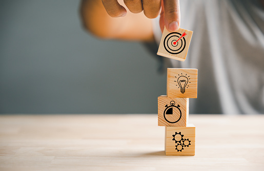 Wood block stacking guided by a businessman's hand symbolizes a strategic business plan and Action plan, emphasizing the concept of goal formation and objective achievement.