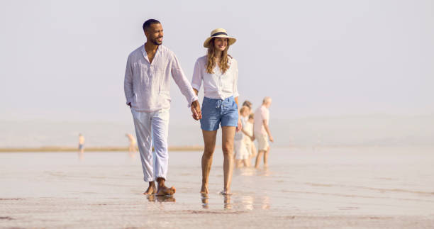 couple walking on beach - women wading sun hat summer foto e immagini stock