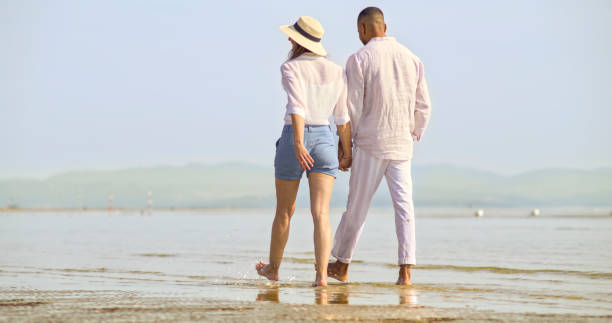 couple walking on beach - women wading sun hat summer 뉴스 사진 이미지