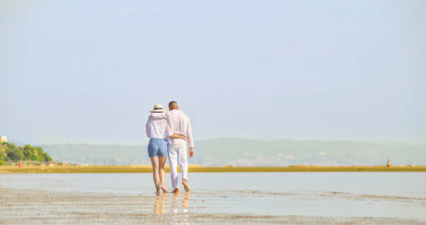 couple walking on beach - women wading sun hat summer 뉴스 사진 이미지