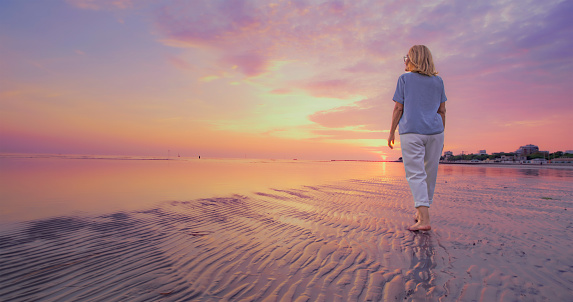 Rear view of senior woman walking on beach during sunset.