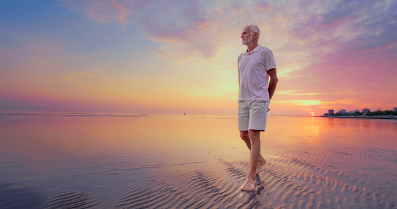 Front view of senior man walking on beach during sunset.