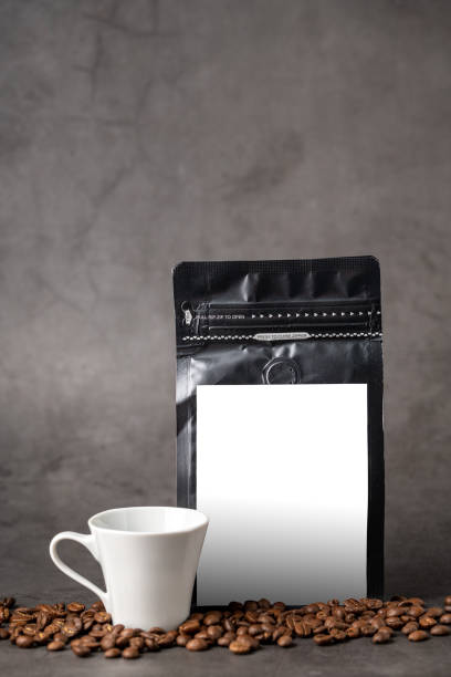 istock Black coffee foil packaging bag and coffee cup with blank white label on stone table 1906335802