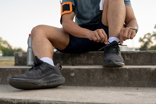 Close-up image of a man in sportswear sitting on the stairs and tying his shoelaces, getting ready to exercise run in a park.