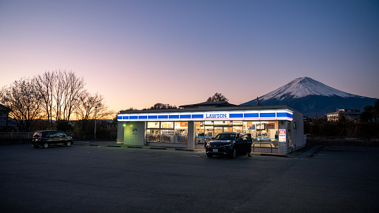 Dusk view of a Lawson convenience store parking lot with Mount Fuji in the backdrop during twilight in Japan.