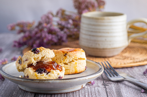 Close-up of traditional British scones on a plate with a tea cup and flower blurred background. Space for text.