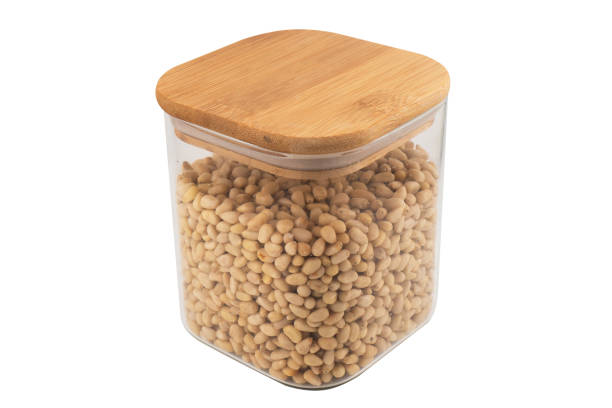 istock Cedar nuts in glass jar isolated on white background. Transparent glass package of pine nuts. Top view 1906431406