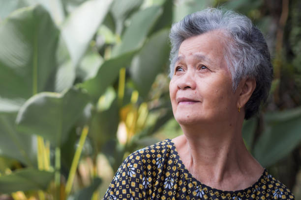 istock Senior woman smiling and looking up while standing in a garden. 1906432932