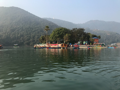 Lake Phewa on the background of a green mountain valley and the snowy top of Mount Annapurna under a blue sky, view from the water. Tal Barahi temple and Himalayas