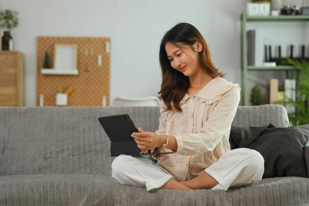 istock Happy young woman dressed in casual clothes sitting on couch and browsing internet on digital tablet. 1906480509
